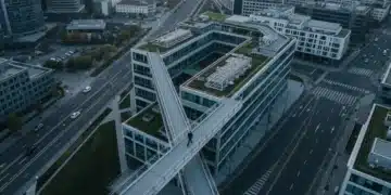 Aerial view of an interconnected urban landscape at dawn, featuring a large coworking space, geometric road patterns, and a lone figure walking a pedestrian bridge, symbolizing the hybrid workforce and gig economy.