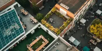 Aerial view of a diverse urban landscape split into geometric segments, showcasing a co-working space, a person working from a balcony, and a bustling street market, symbolizing the fractured yet interconnected modern workforce. Golden hour light illuminates green accents and rich textures.