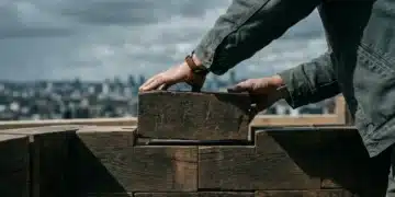 Person carefully building a foundation with reclaimed wooden bricks, symbolizing sustainable startup growth and resilience.