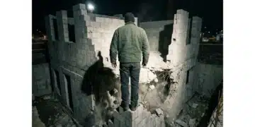A person in a dark green jacket stands before a rapidly built concrete structure with a crumbling foundation, illustrating premature startup scaling.